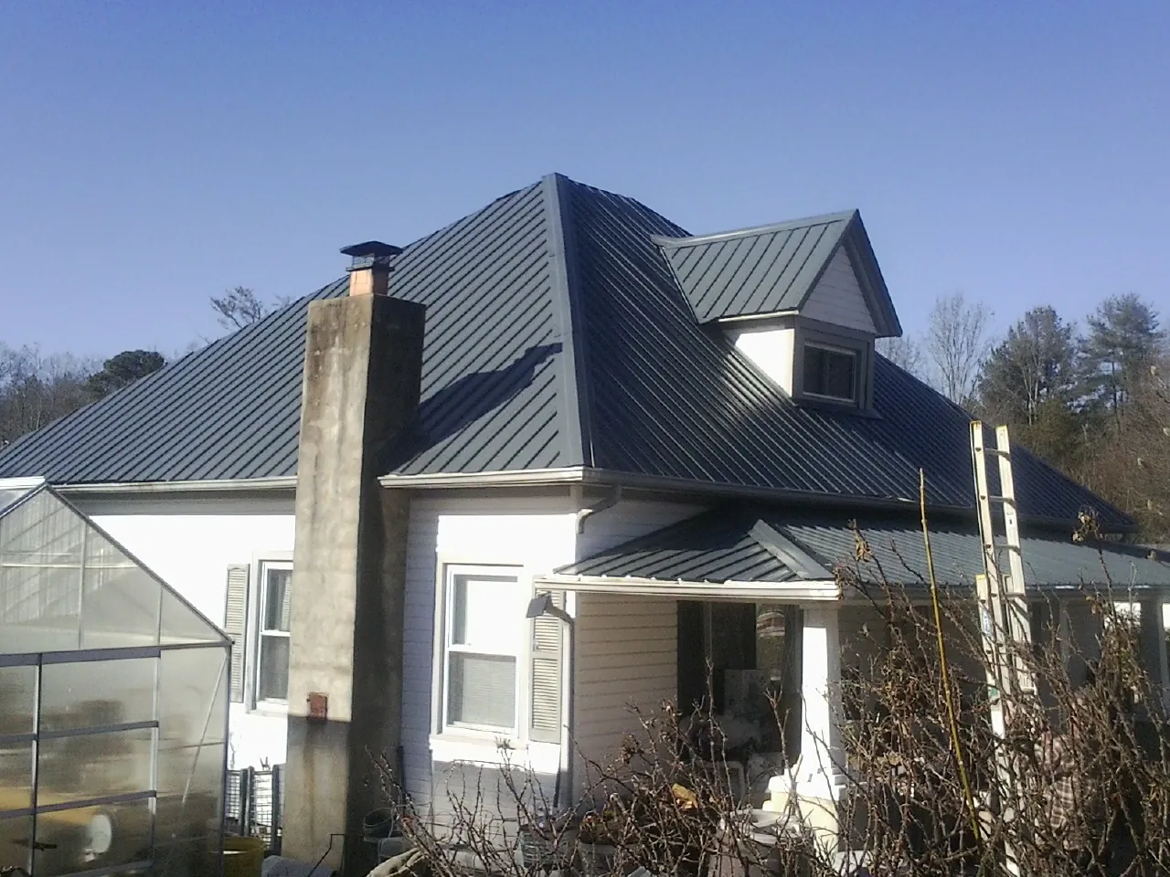 Dark blue standing seam metal roof on a white farmhouse with dormer — Slate & Tile Roof Repair by Roofing Brothers in Binford