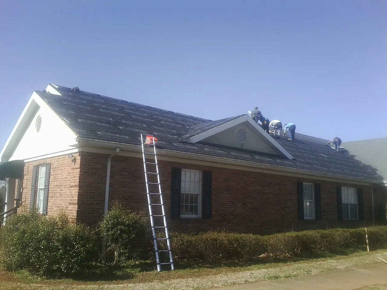 Crew tearing shingles off a brick ranch roof with a ladder set — Emergency Roof Repair work by our crew in Binford