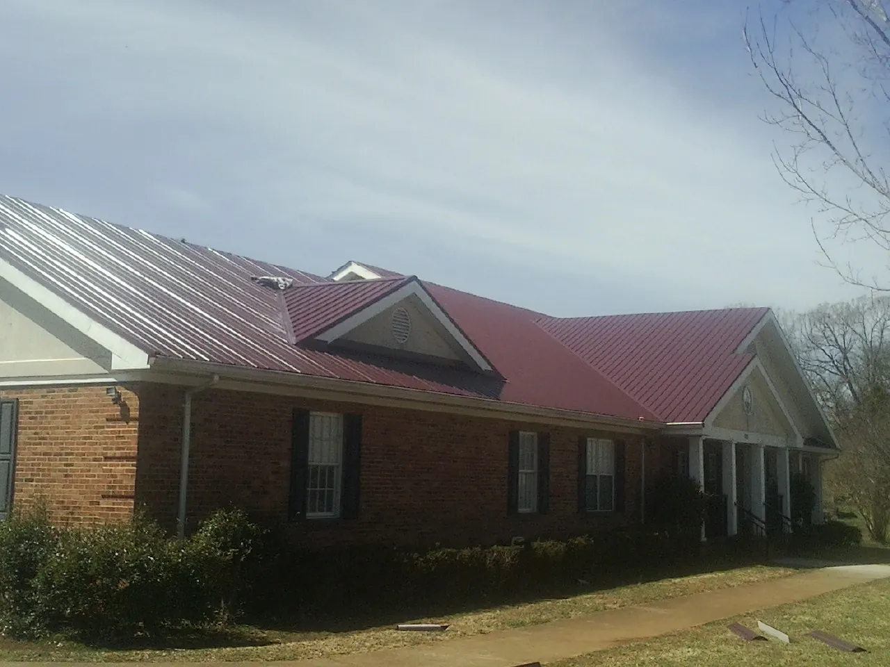 Red metal roof with gabled entries on a long brick building, from a Hail Damage Roof Repair job in Binford