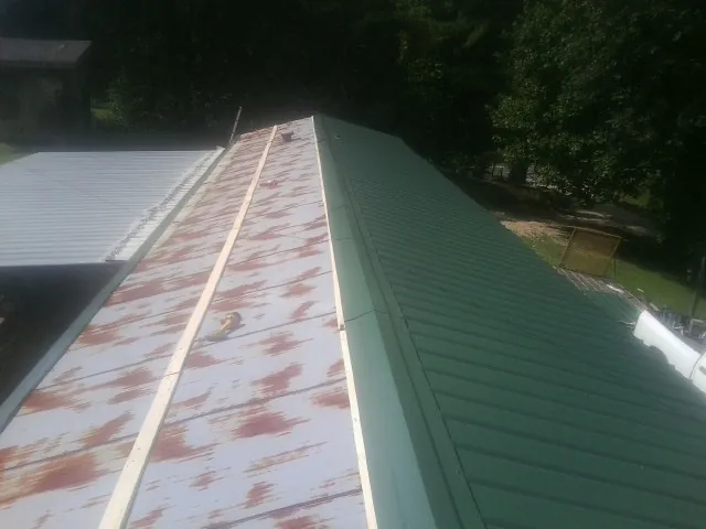 Old rusted panels beside newly installed green metal roofing — Wind Damage Roof Repair by Roofing Brothers in Binford
