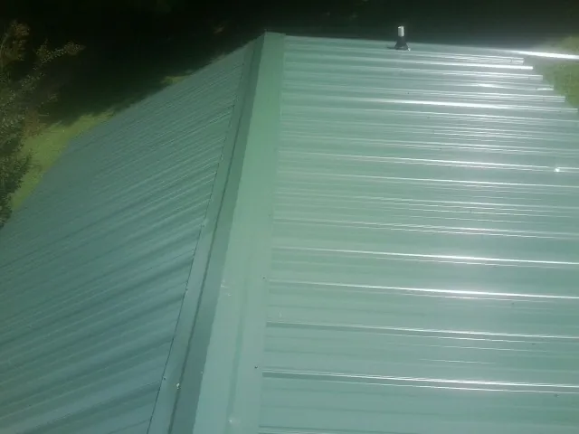 New green metal panels meeting at the ridge of a roof — Flat Roof Repair work by our crew in Binford
