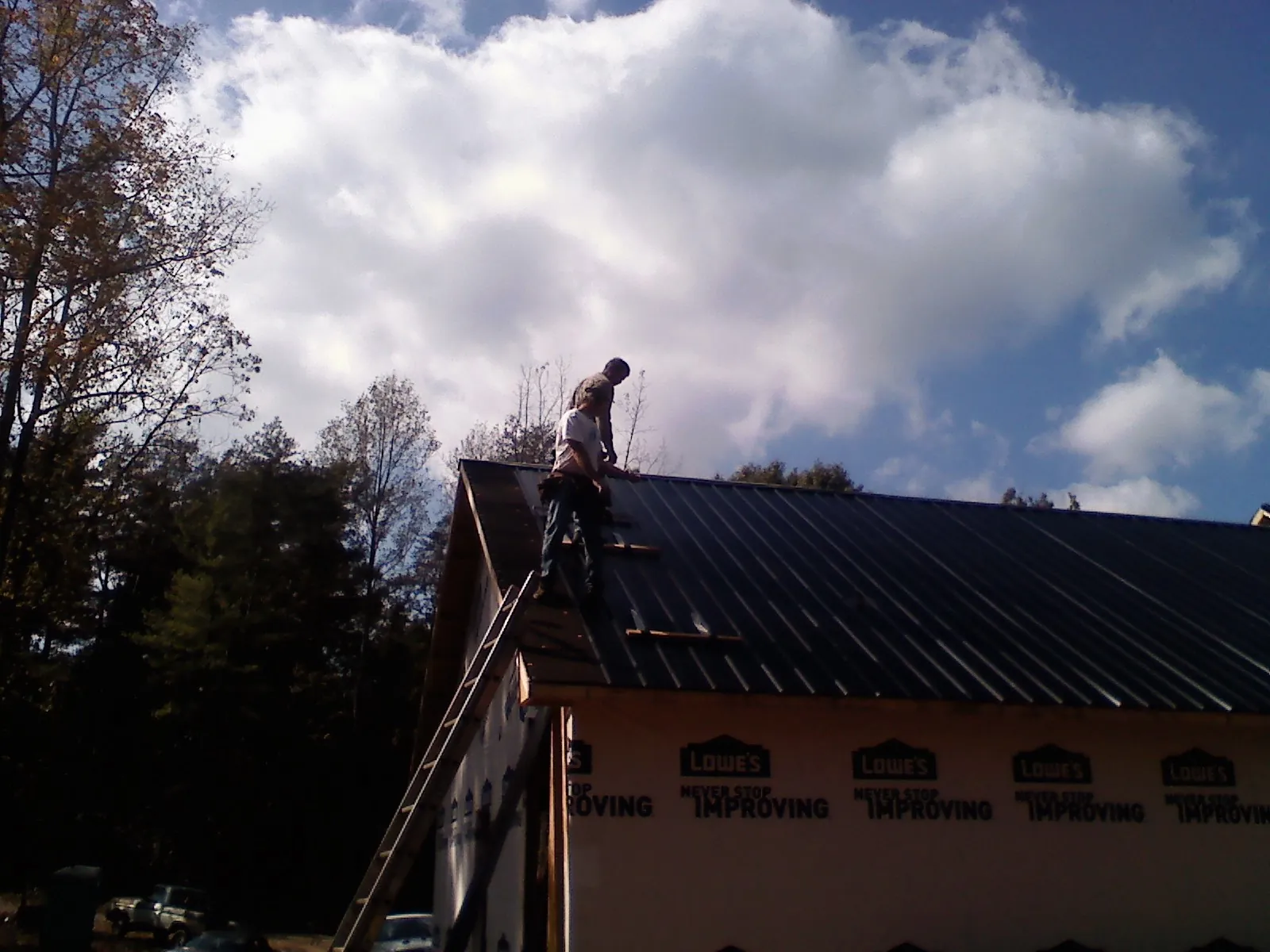 Roofer fastening dark metal panels high against a cloudy sky, from a Roof Inspection job in Binford